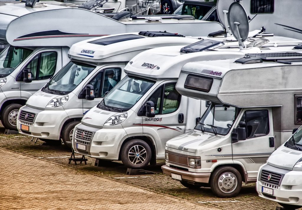 Mehrere Wohnmobile parken in einer Reihe nebeneinander auf einem Campingplatz.