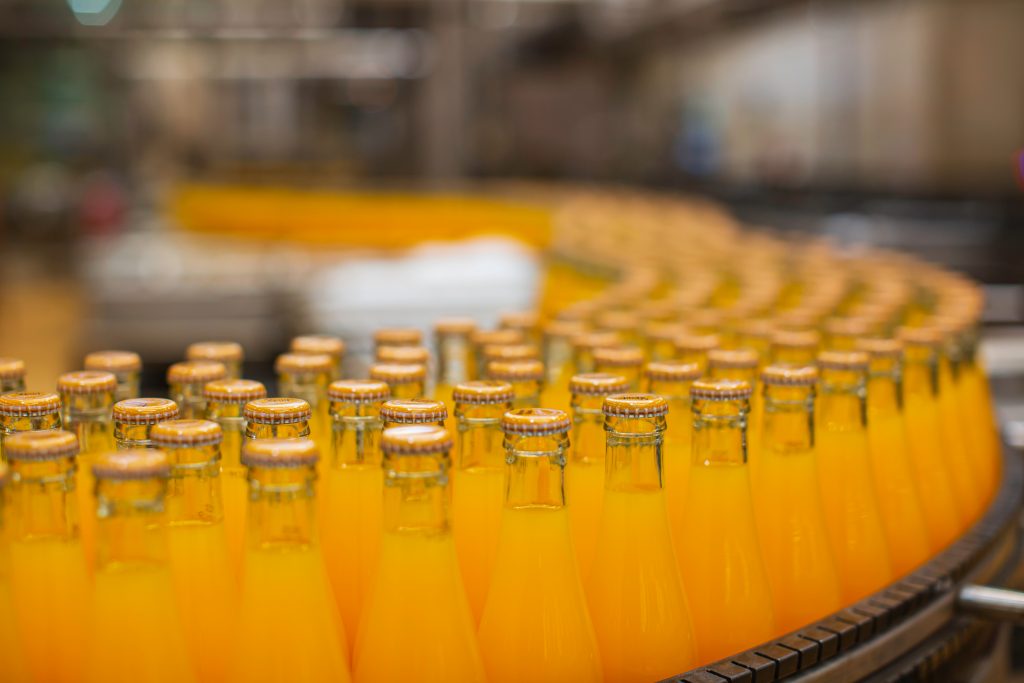 Ein Laufband voller Glasflaschen, die mit einem orangenen Getränk gefüllt sind.